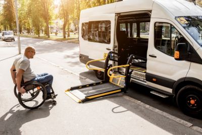 Personne en fauteuil roulant montant à bord d'un véhicule adapté TPMR.
